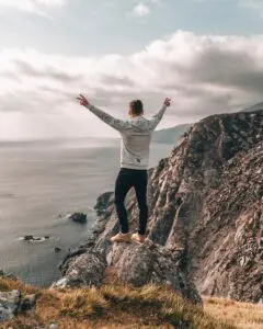 man in white dress shirt standing on brown rock formation near body of water during daytime