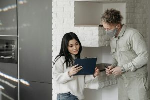 Masked courier and woman interacting indoors, highlighting safe delivery practices.
