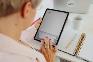 Woman writing notes on a tablet in a modern workspace with notebooks and a coffee cup.