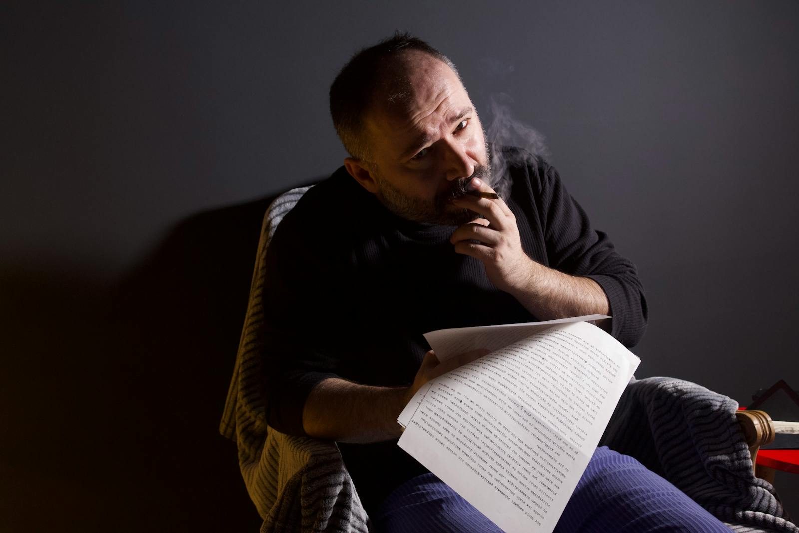 Thoughtful man reviews script while smoking indoors, set in Ankara.