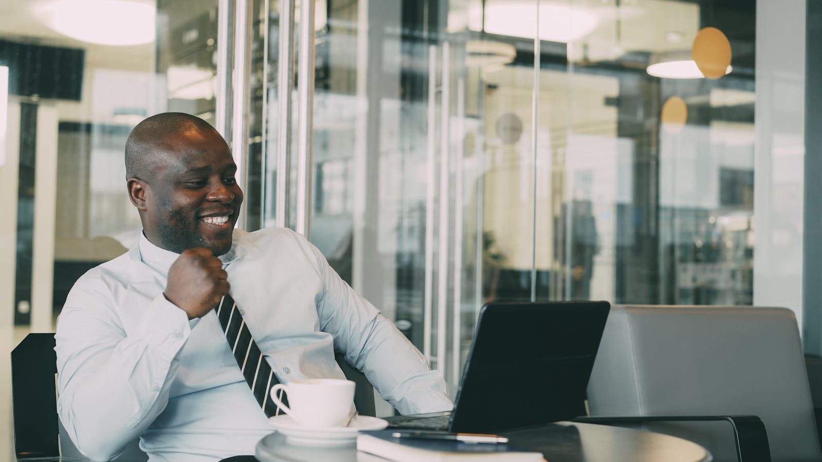 Confident businessman celebrating success while working on a laptop in a modern office setting.