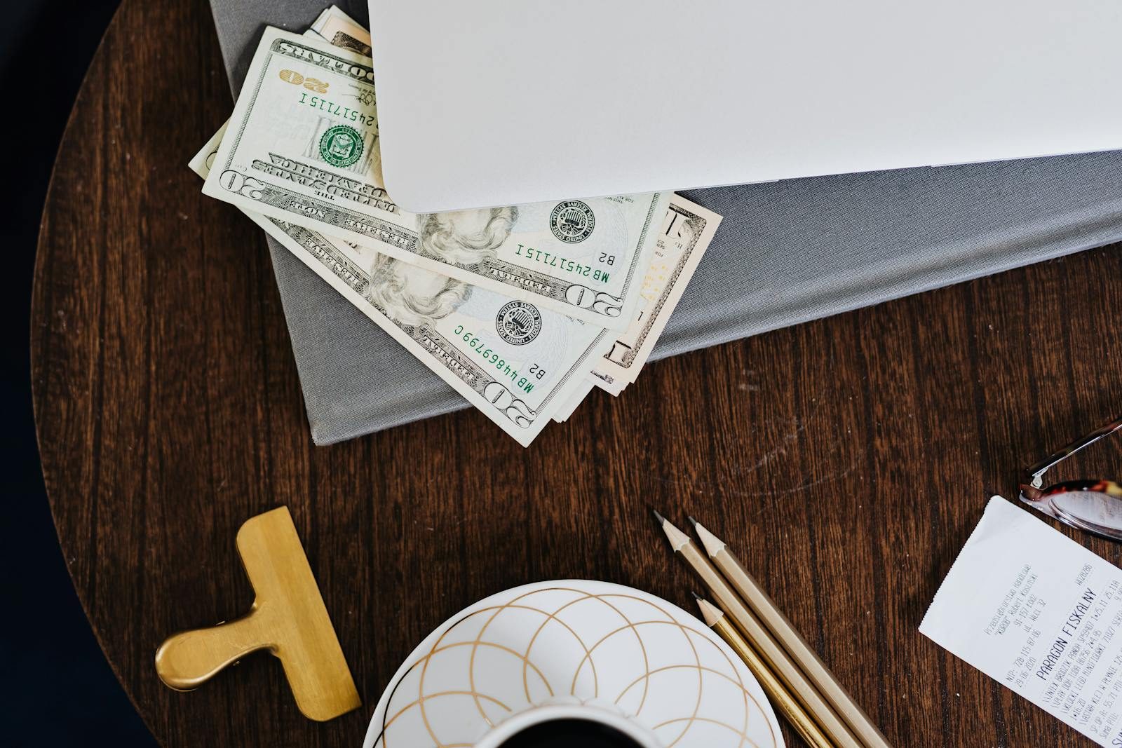 Stylish workspace featuring coffee cup, dollar bills, laptop, and stationery on a wooden table.