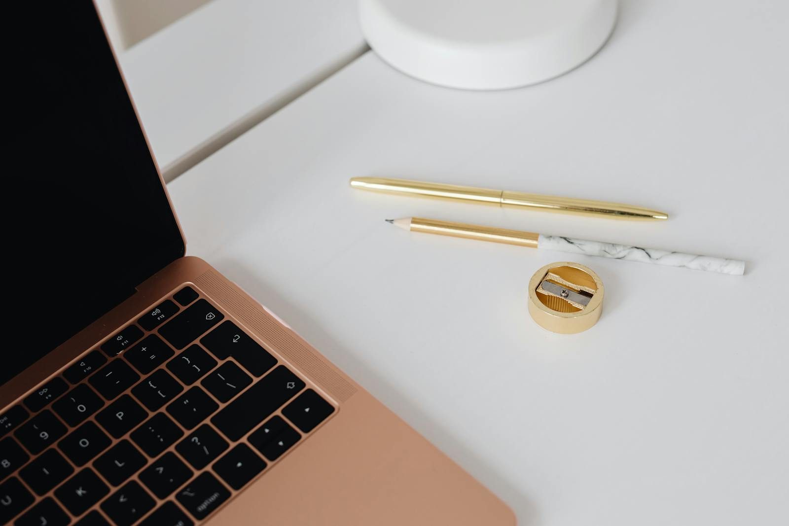 Elegant workspace featuring a gold pen, marble pencil, sharpener, and laptop on a white desk.