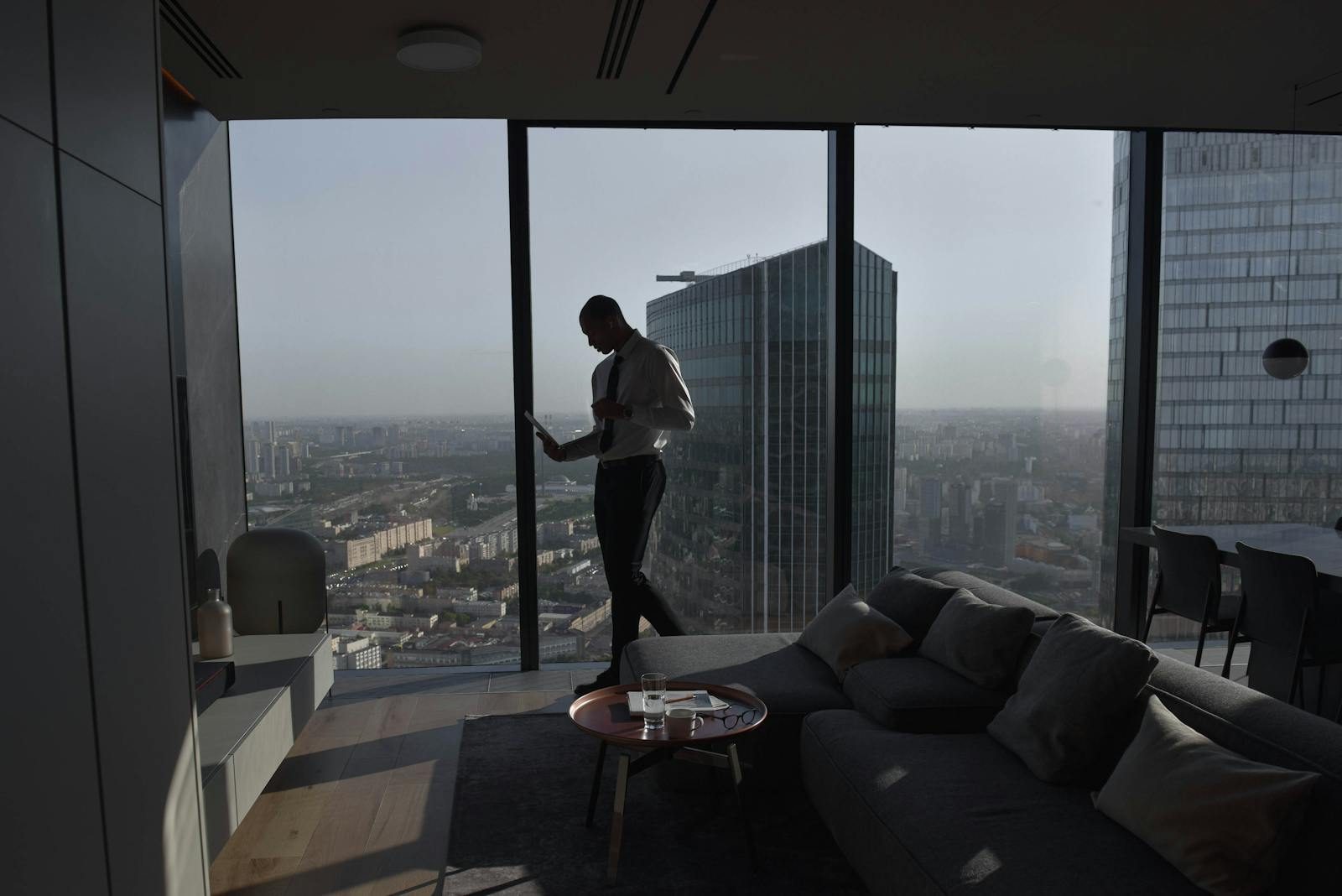 Silhouette of a businessman standing in a luxury apartment with a panoramic cityscape view.