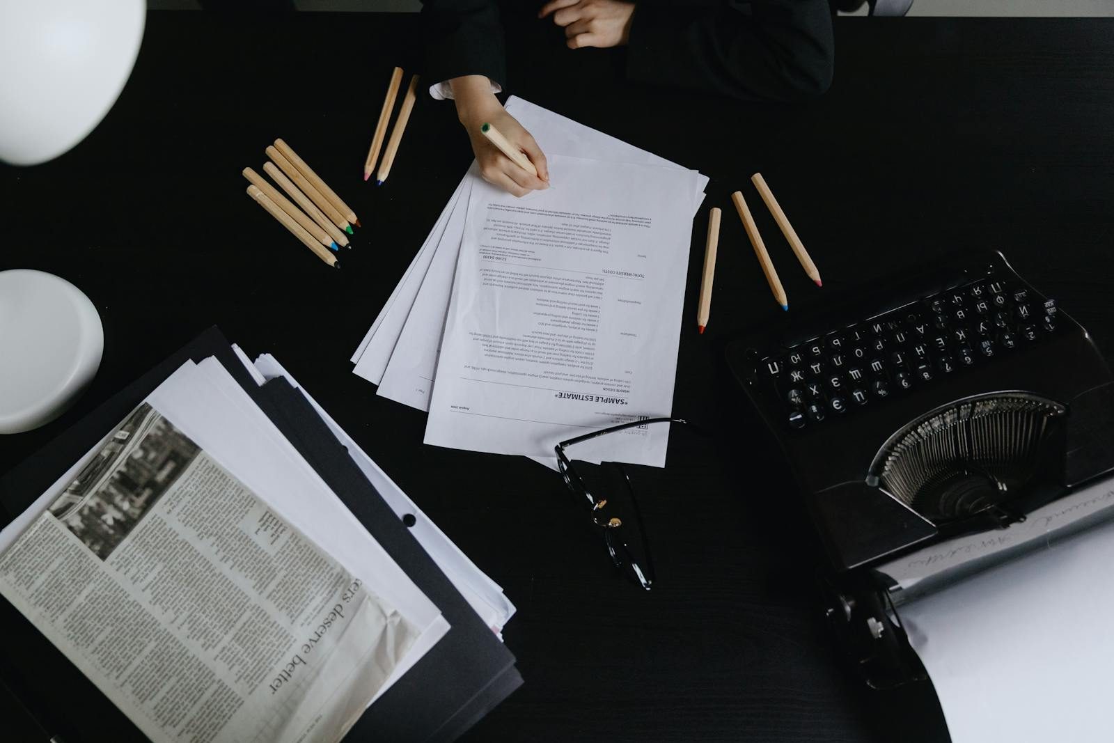 Aerial shot of a desk with papers, typewriter, and colored pencils, creating an organized and vintage workspace vibe.