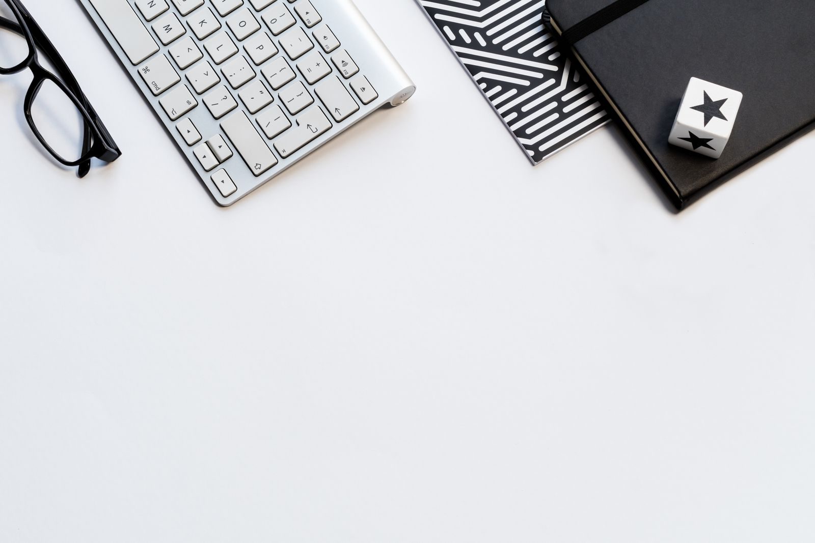 A stylish home office flat lay with a keyboard, glasses, and notebooks on a white backdrop.