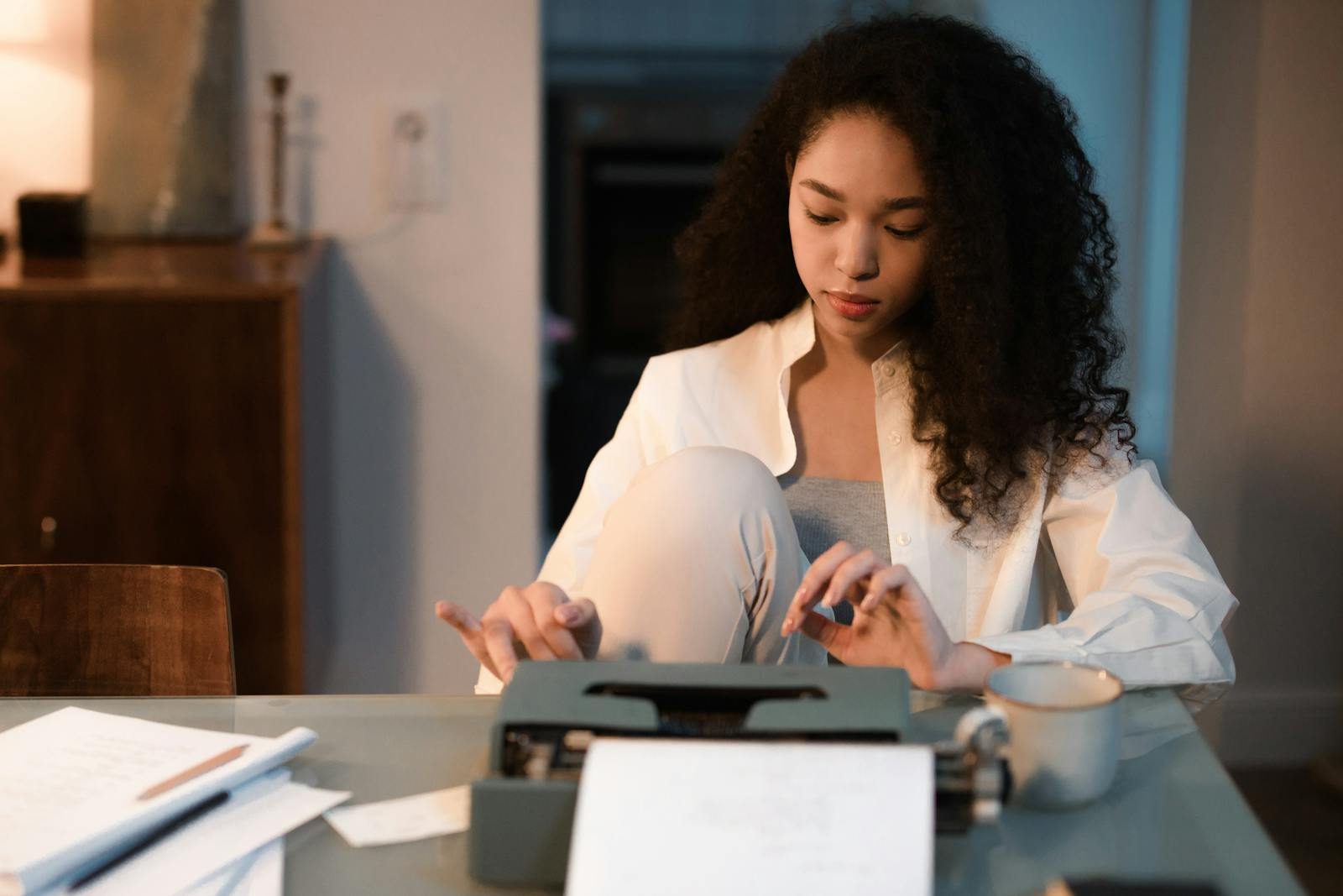 A young woman typing on a vintage typewriter at a desk with papers indoors.