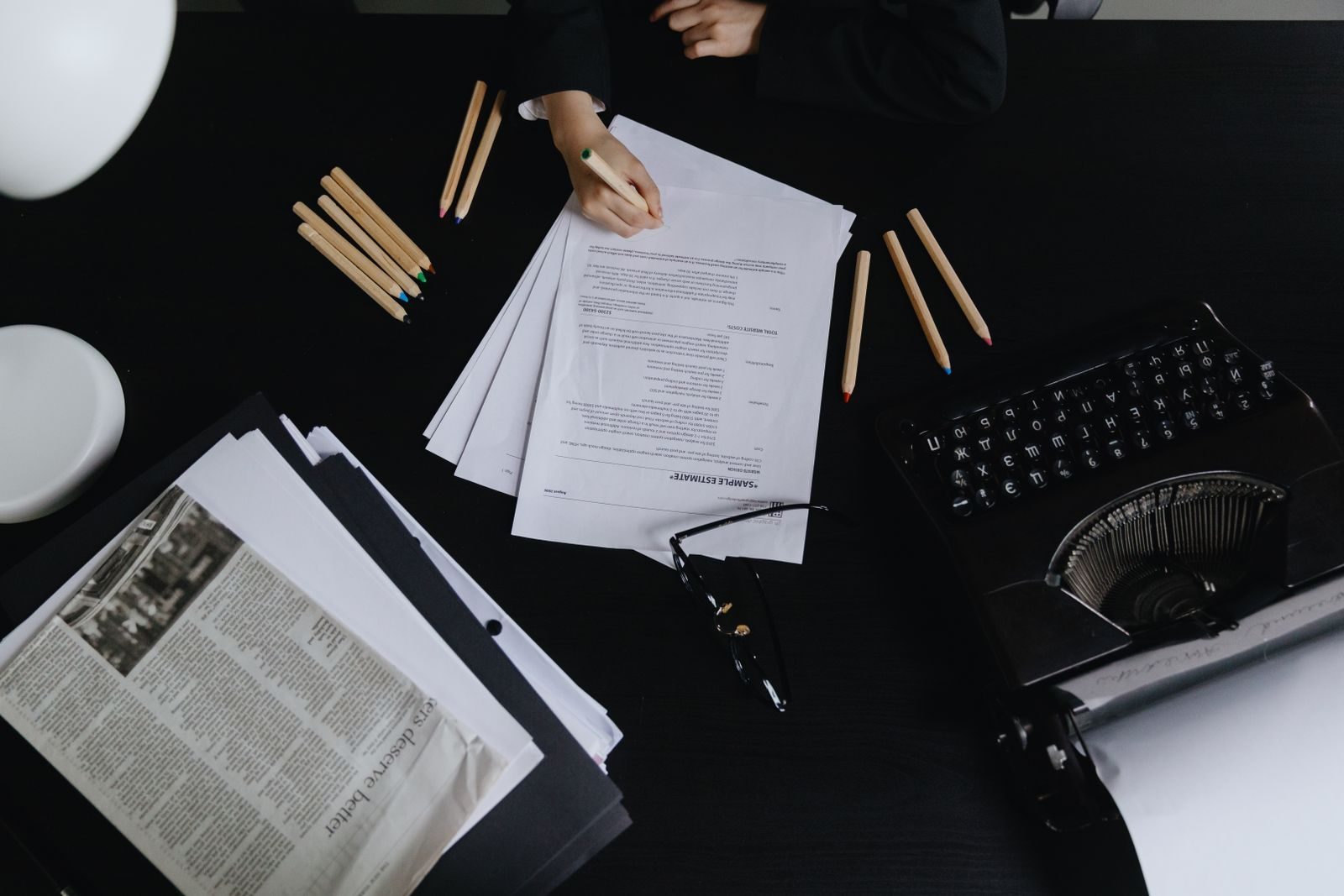Aerial shot of a desk with papers, typewriter, and colored pencils, creating an organized and vintage workspace vibe.