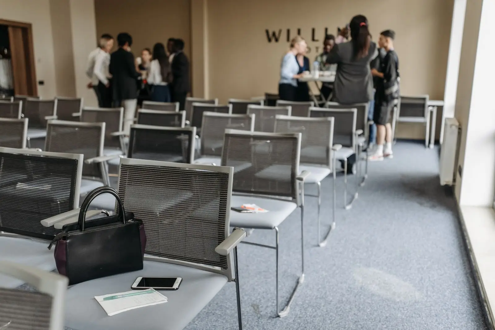 An empty conference room with chairs and a group of people gathered at the back.