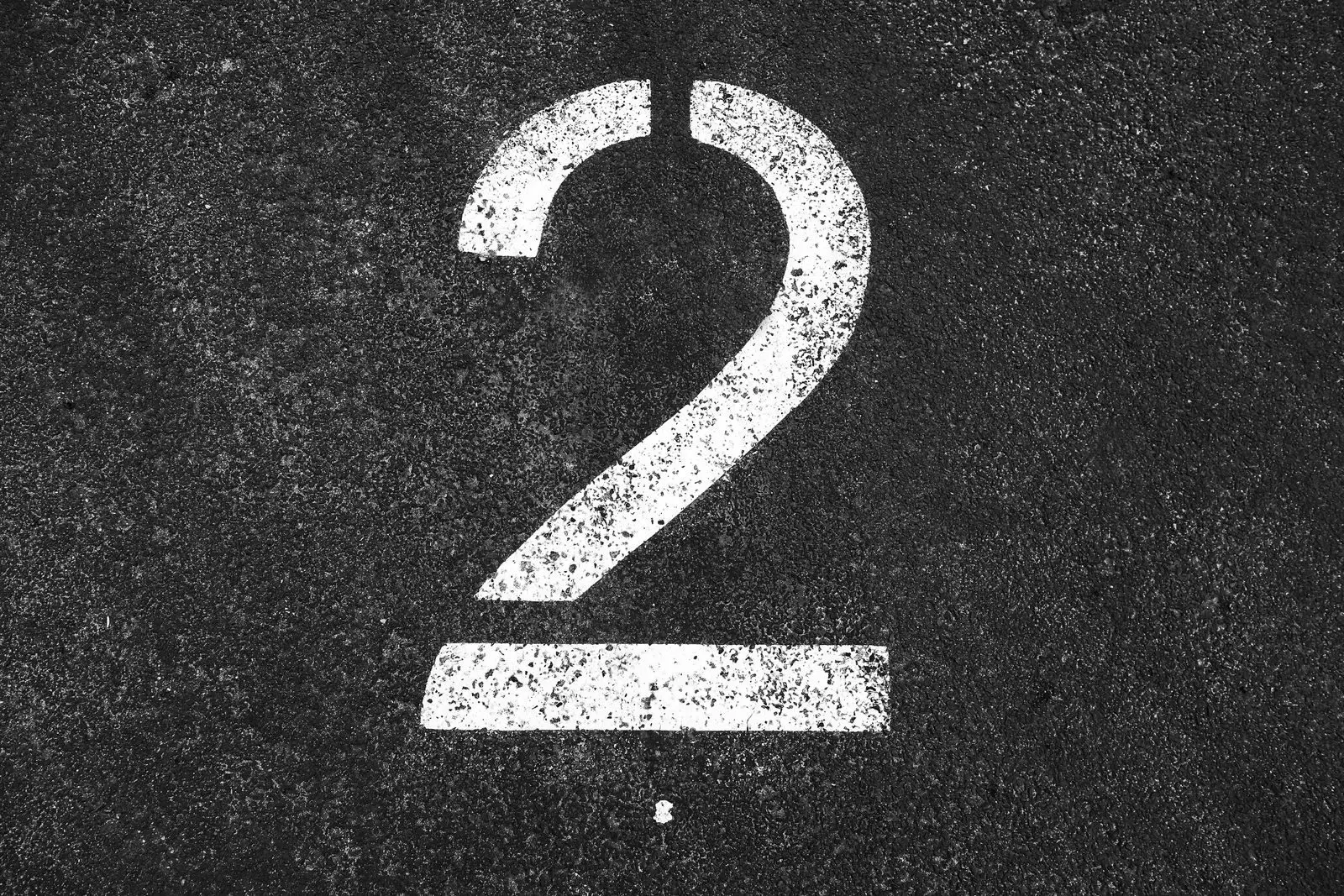 Close-up of a large white number two painted on a textured asphalt surface.