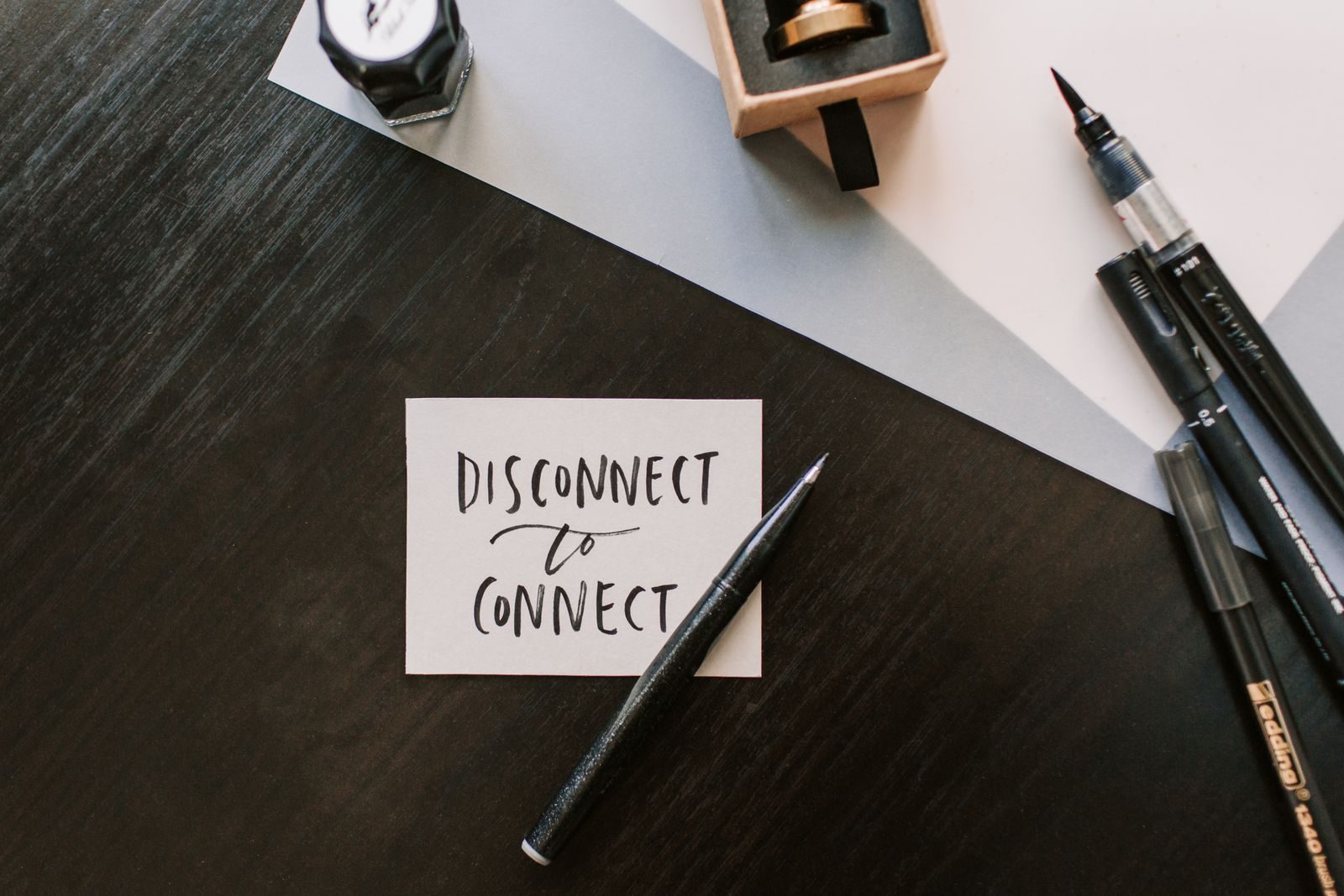 A flat lay image featuring a handwritten note with pens on a wooden surface, promoting mindful connection.
