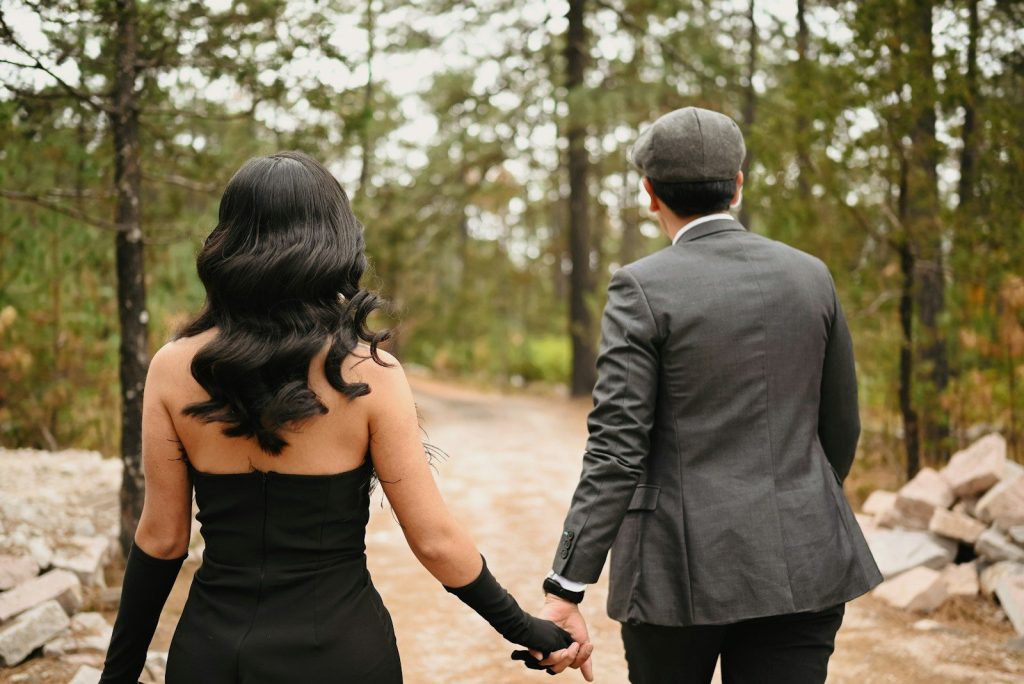 Two people holding hands walking away on a dirt path through pine trees