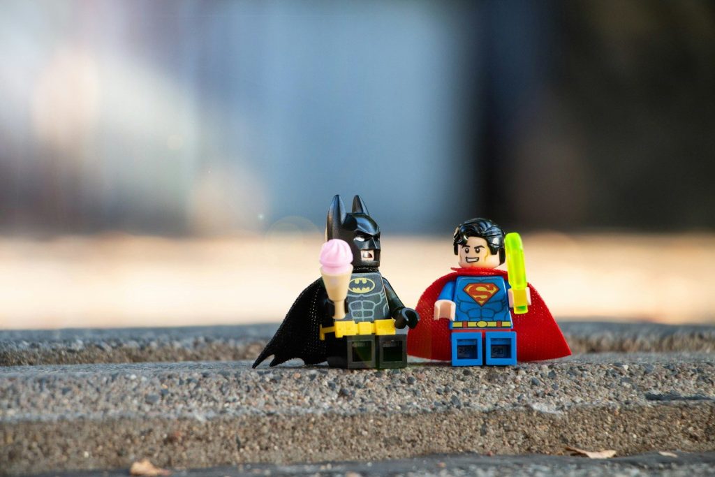 Batman and Superman Lego minifigures with ice cream and a light saber on concrete